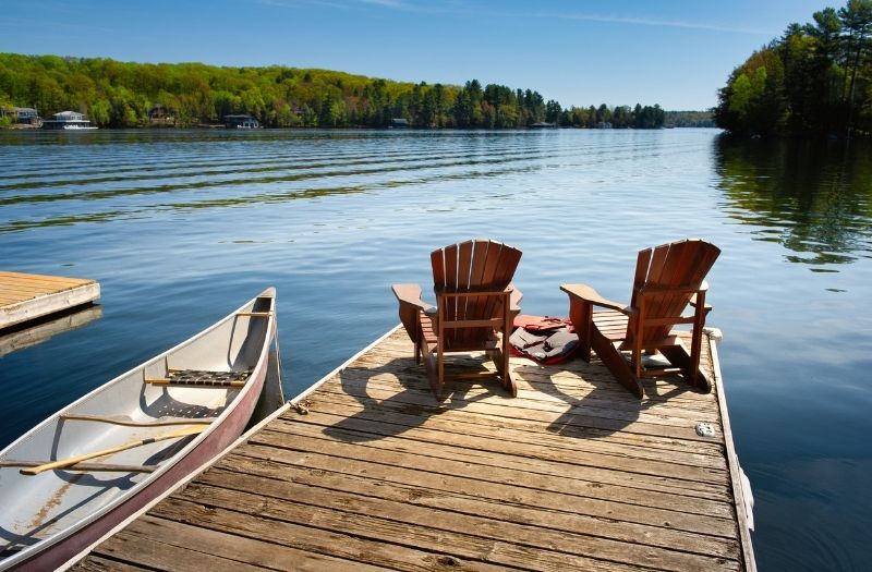 Two Adirondack chairs on a wooden dock facing the blue water of a lake in Minnesota.
